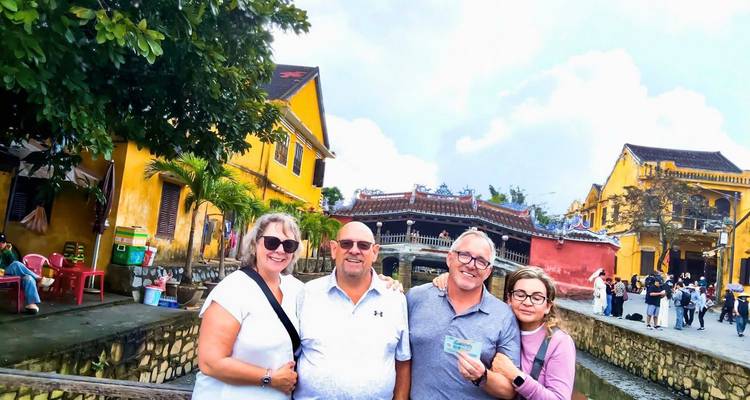 Four tourists posing beside a small canal and bright yellow heritage houses in an old town street.