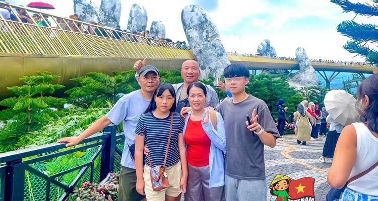 Family smiling in front of the famous Golden Bridge with giant stone hands and lush greenery.