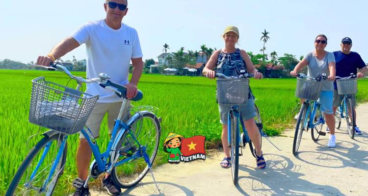 Four cyclists standing with blue bikes on a path next to bright green rice paddies.