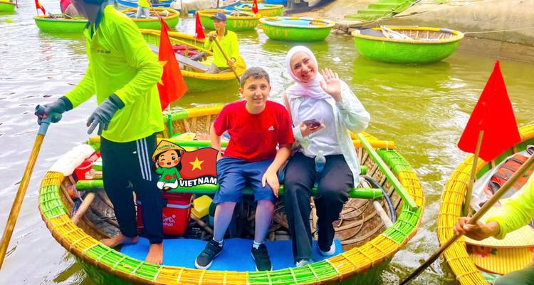 Mother and son waving from a colorful round basket boat on a green river while guides paddle nearby.