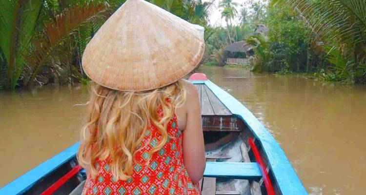 Back view of a person in a wooden boat amidst tropical lush waterways.