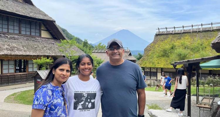 Familia posando con casas tradicionales de techo de paja y una montaña al fondo.