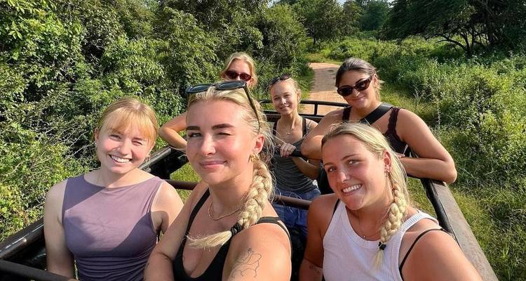 Group photo on a safari vehicle, with greenery around.