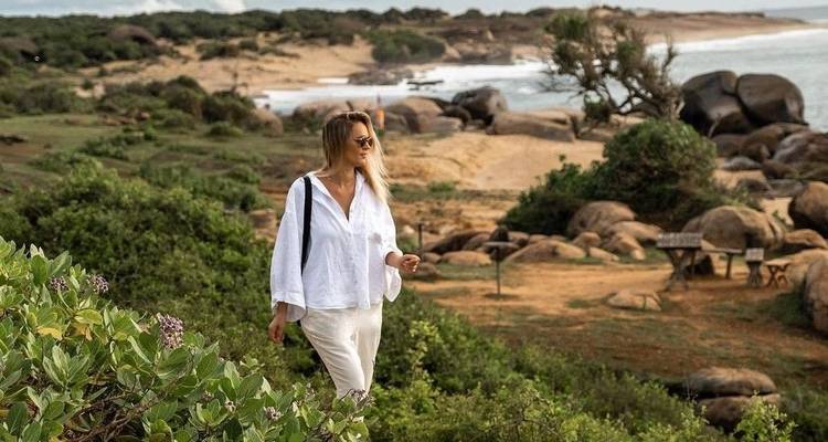 Woman stands amidst lush landscape near the ocean.