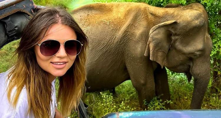 Woman posing with an elephant in a wildlife setting.