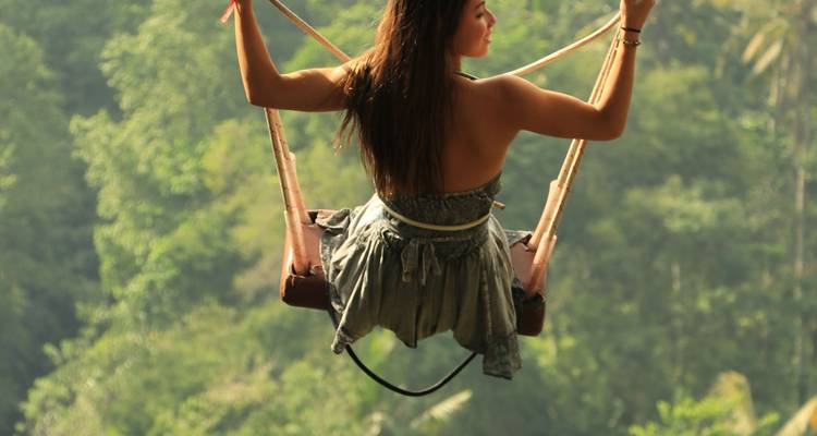 Woman on a swing high above lush forest scenery.
