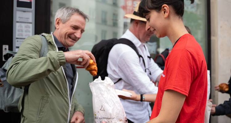 Tour guide in a red shirt handing a fresh croissant to a smiling traveller during a street food tour.