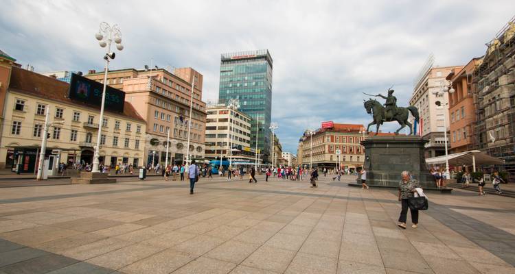 Place de ville animée avec des cafés et une statue d'un cavalier.