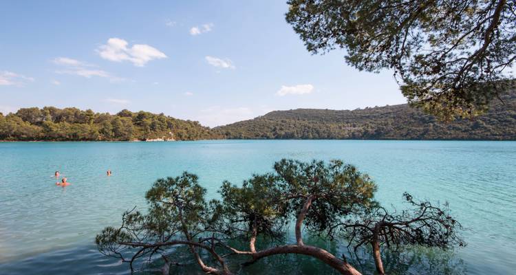 Calm turquoise lake with swimmers and dense forest on the shore.
