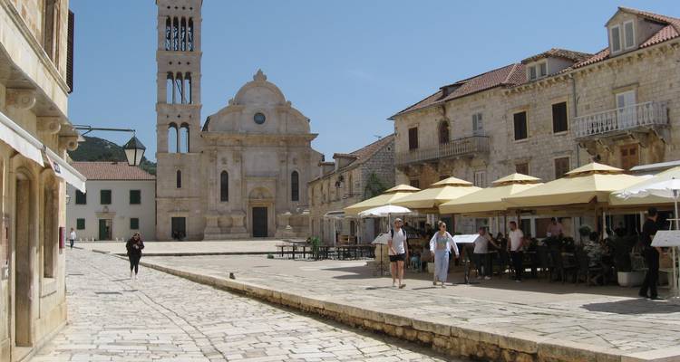 Historic town square with walking tourists and a stone church tower.