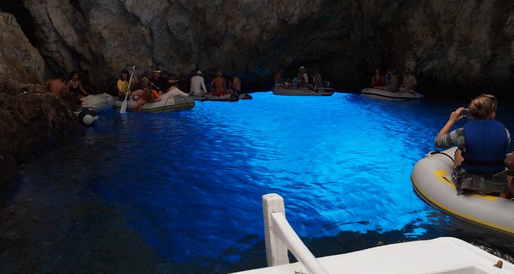 Tourists in boats exploring a luminous blue water cave.