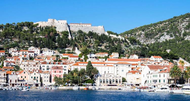 Pueblo costero con murallas de fortaleza y vegetación alrededor.