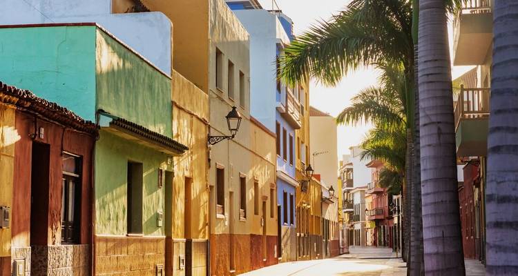 Bunte Gebäude säumen eine palmengesäumte Straße mit warmem Licht.