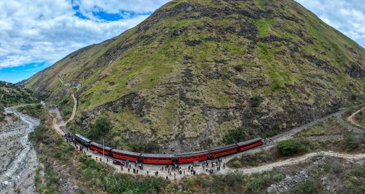 Vue panoramique d'un long train voyageant le long d'un sentier montagneux.