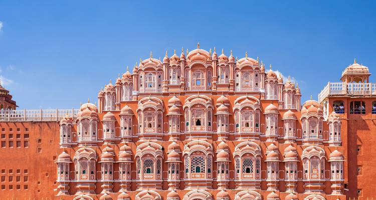Fachada ornamentada de piedra arenisca rosa de un edificio histórico bajo un cielo despejado.