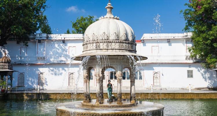 White marble pavilion surrounded by fountains in a garden.
