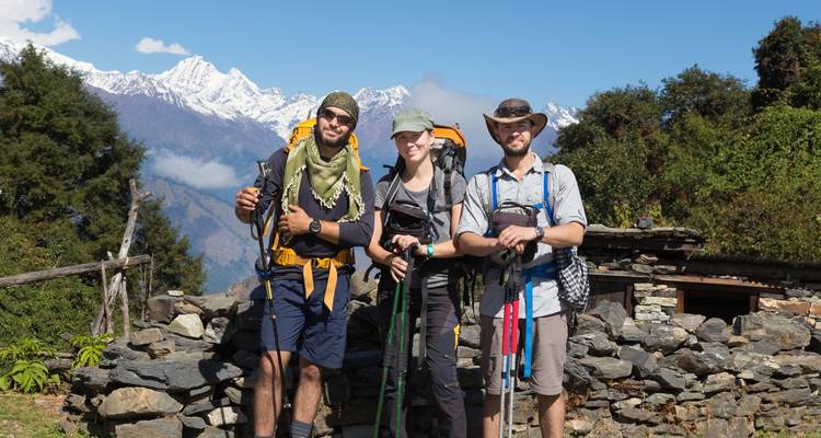 Drei Wanderer posieren mit Trekkingstöcken vor Bergen.