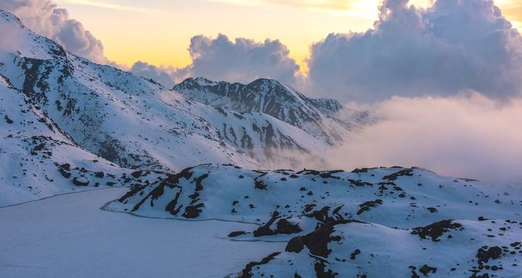 Schneebedeckte Berge bei Sonnenuntergang mit dramatischen Wolken.