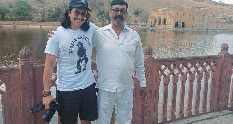 Deux hommes posant près d'une balustrade avec un plan d'eau en arrière-plan.