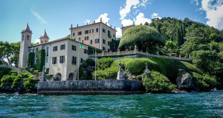 A grand villa on a lakeside surrounded by lush greenery.
