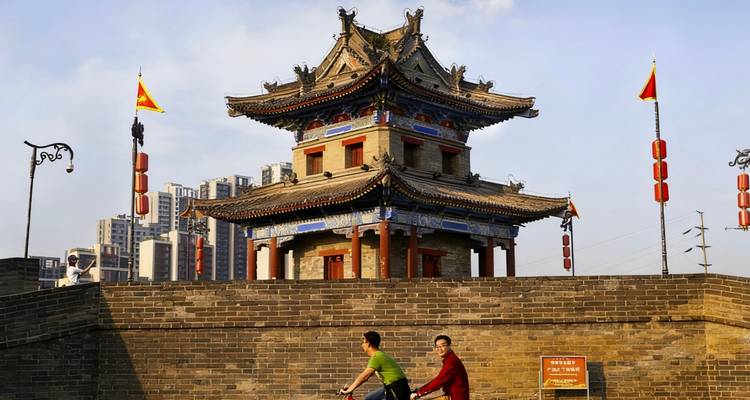 Two people cycling past a traditional Chinese gate.