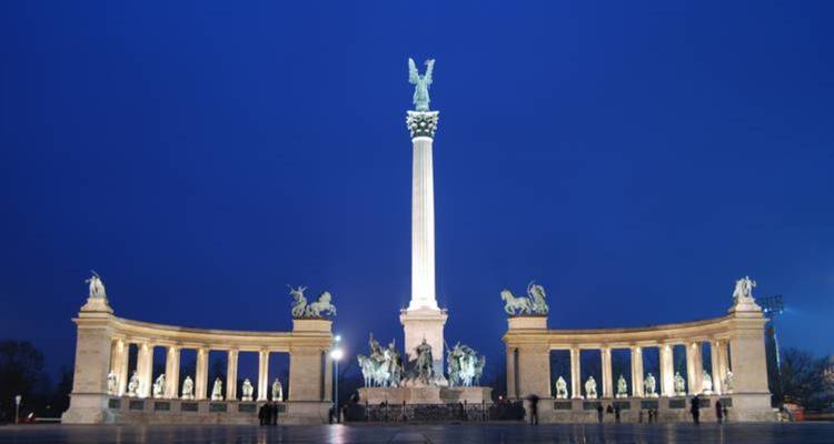 Un grand monument avec des statues et une colonne illuminé la nuit.