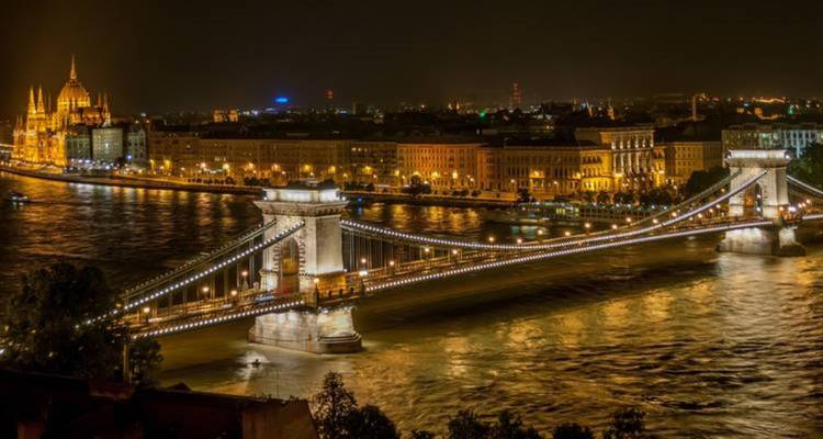 Un pont magnifiquement éclairé au-dessus d'une rivière avec un horizon urbain.
