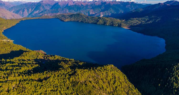 Aerial view of a large lake surrounded by forested mountains.