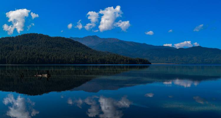 Peaceful lake with mountain reflections under a clear blue sky.