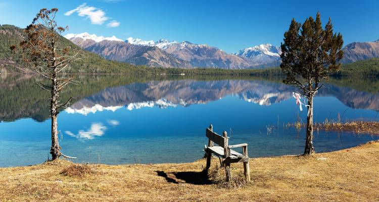 Tranquil lake with mountains and a bench in the foreground.