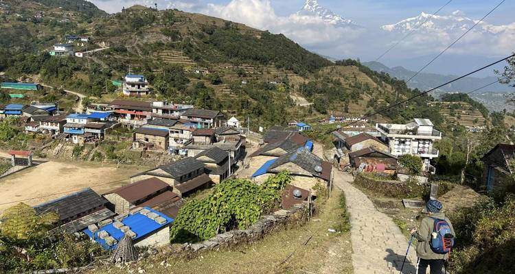 A village with scattered houses and Himalayan mountains in the background.