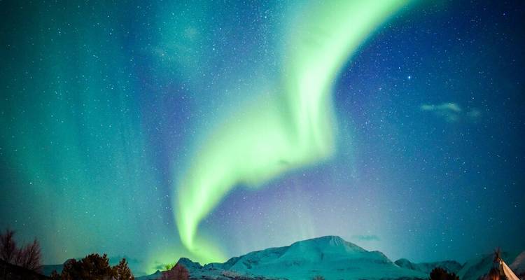 Des arcs aurores boréales d'un vert éclatant traversent un ciel nocturne étoilé au-dessus de pics enneigés.