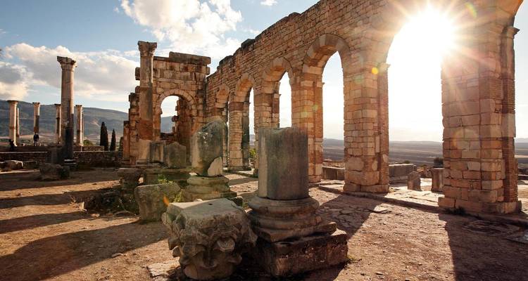 Ruines antiques avec arches et piliers baignées de soleil.