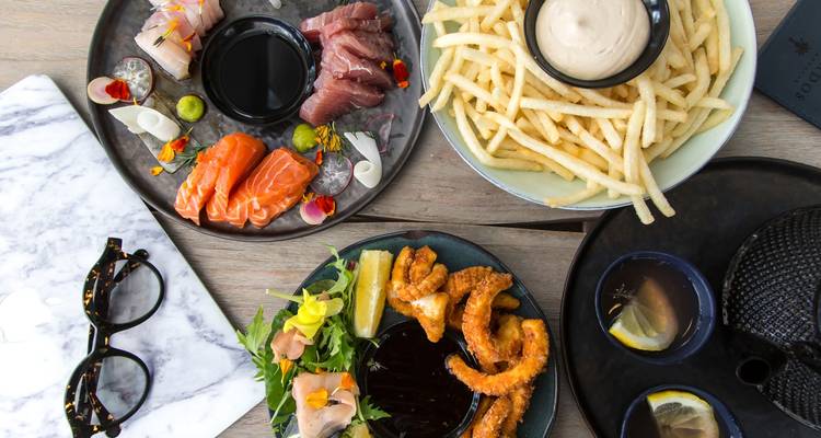 Verschillende gourmetgerechten waaronder sushi, friet en calamari uitgestald op een houten tafel