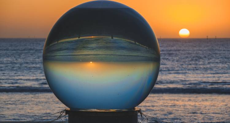 Glass sphere art installation captures an inverted sunset over the calm ocean horizon.