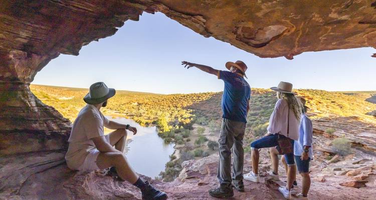 Friends gaze over a winding river from a rocky cave overlook in golden late-day light.