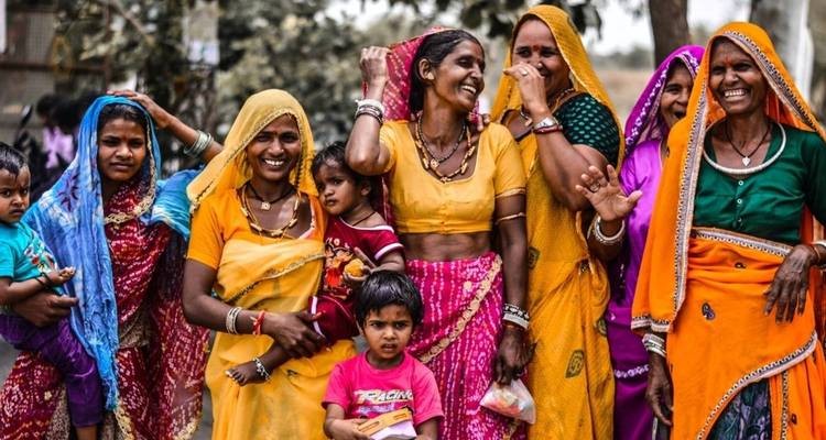 Group of women in colorful traditional clothing laughing and posing.