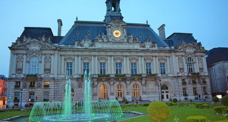 Historic city hall building with a fountain at dusk.