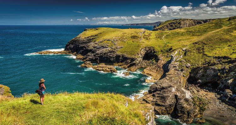 Person standing on a cliff overlooking the ocean and rugged coastline.