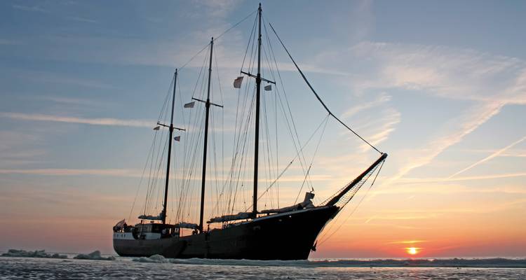 Segelschiff auf ruhigem Wasser bei Sonnenuntergang mit lebhaftem Himmel
