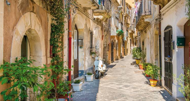 Une ruelle étroite dans une ville italienne avec un scooter garé.