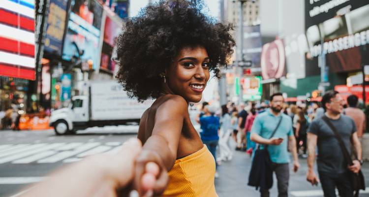 Glimlachende persoon die handen vasthoudt in een drukke stadsstraat.
