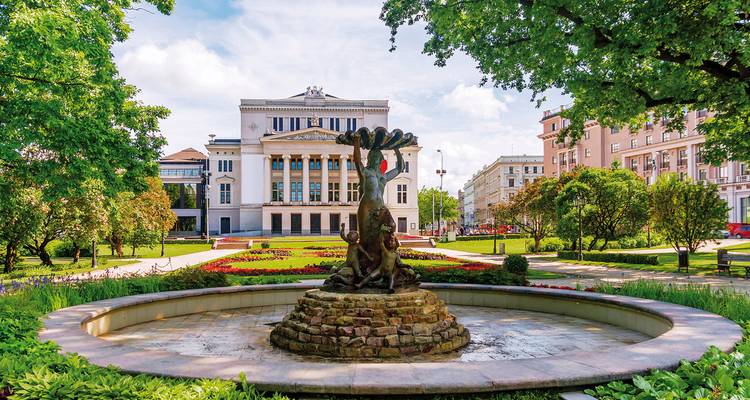 Ein Brunnen vor einem prächtigen Gebäude mit verzierter Fassade, umgeben von Gärten.