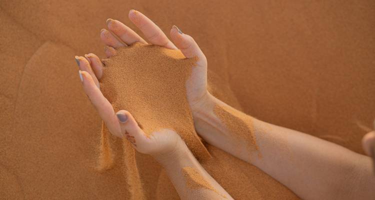 Two hands holding and letting sand fall in a desert setting.