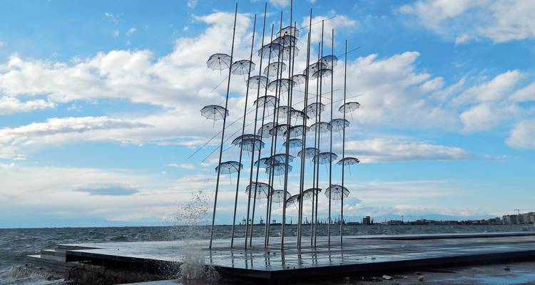 Art installation of umbrellas by the sea with splashing waves.
