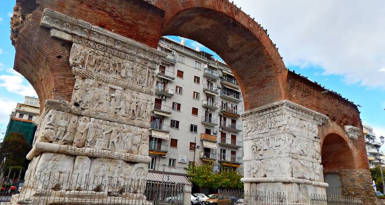 Ancient archway with detailed carvings in an urban setting.