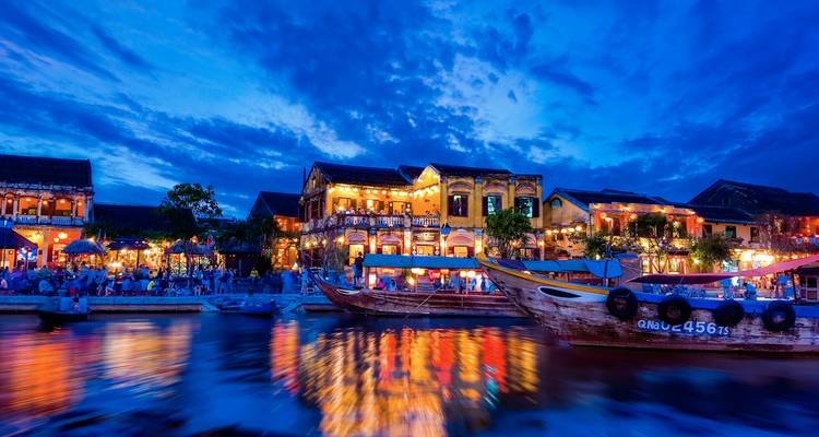 Vue nocturne d'un bord de rivière avec des lumières colorées et des bateaux.