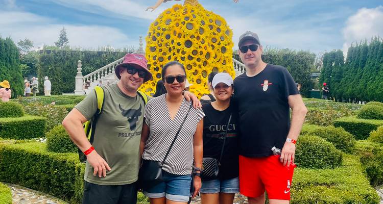Quatre voyageurs souriants devant une sculpture de paon florale jaune vif dans des jardins soignés
