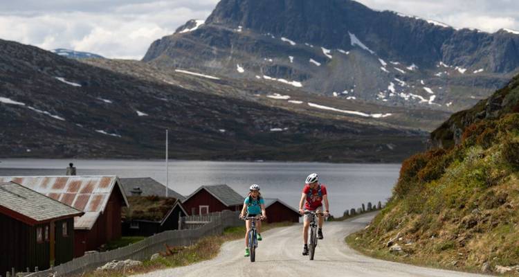 Dos ciclistas en una carretera montañosa pintoresca sobre un lago.
