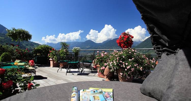 Terraza en la azotea llena de flores con sillas de descanso que da a exuberantes valles alpinos y montañas distantes.